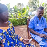 A doctor consults the prescription on his tablet and delivers drugs to his elderly patient in Africa